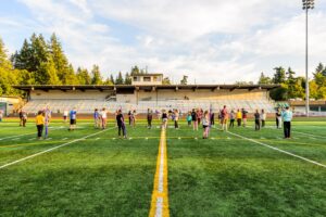 Marching band students practice on a football field, spaced across the yard lines during an afternoon rehearsal.