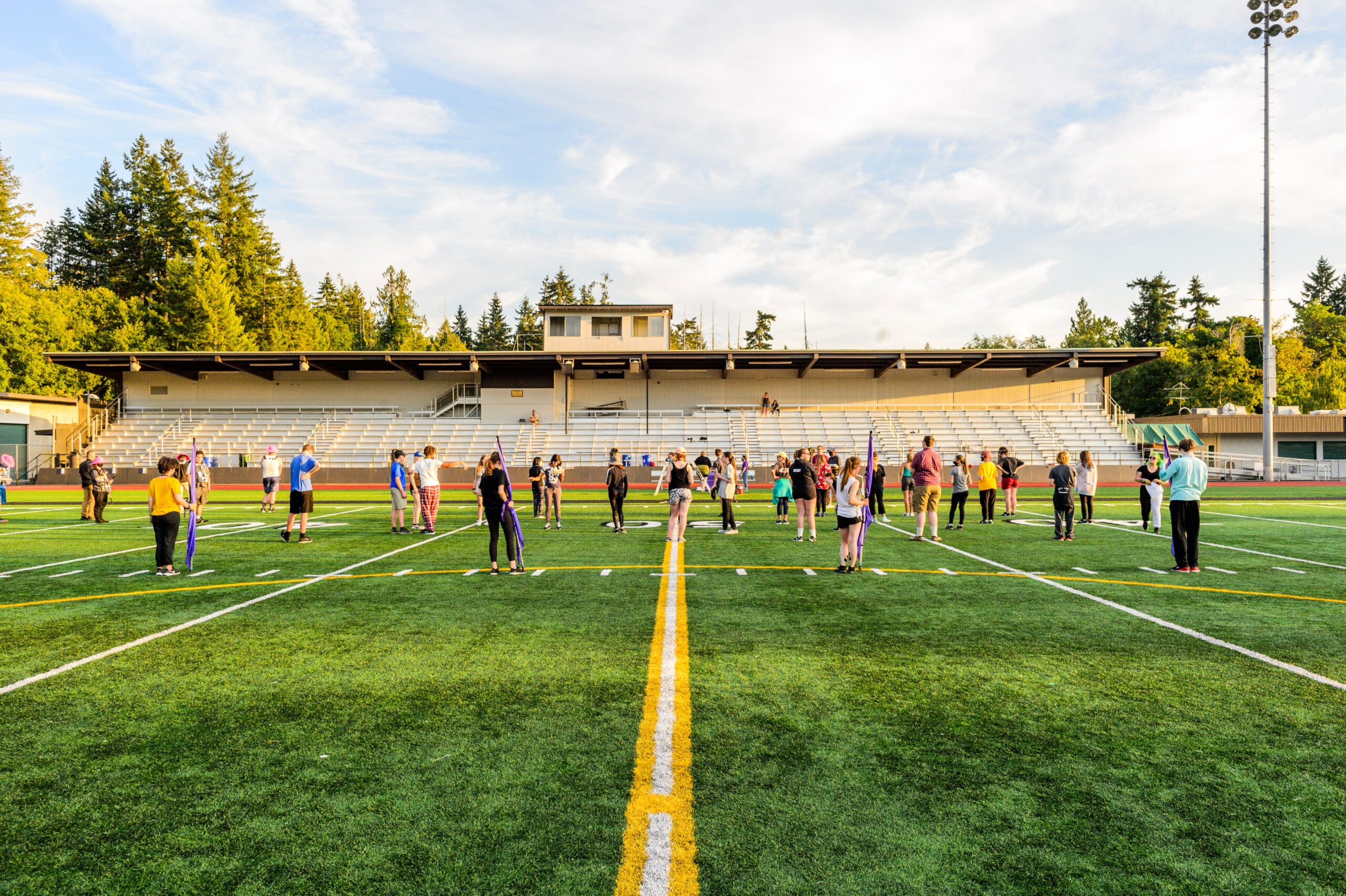 Marching band students practice on a football field, spaced across the yard lines during an afternoon rehearsal.